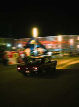 Retro automobile driving through city streets at night in Bakü, capturing nostalgia and motion.