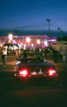 A vintage car on the bustling streets of Baku at night, surrounded by city lights and energy.