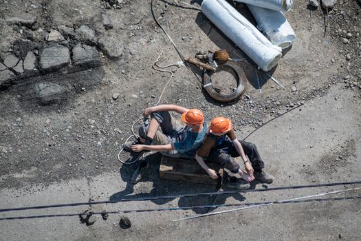 Two construction workers in hard hats rest on a site, viewed from above.