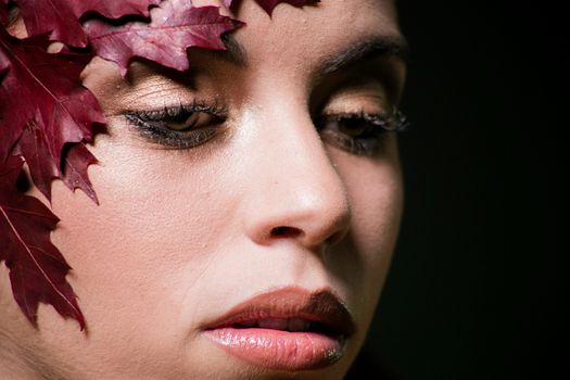 Artistic close-up portrait of a woman with red leaves on her forehead, showcasing beauty and nature.