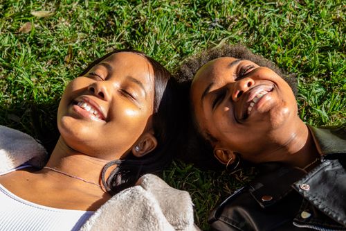 Free Two women lie on grass, smiling in sunlight. Captures joy and friendship. Stock Photo