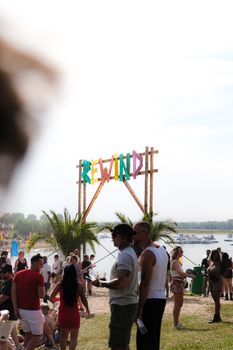 Lively summer festival by lakeside with a diverse crowd enjoying the day.
