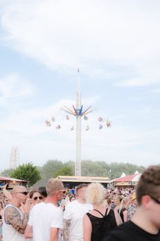 A vibrant festival scene with a thrilling funfair ride and a bustling crowd under a clear sky.