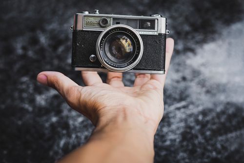Free Close-up of a classic vintage camera held in a hand against a textured dark background. Stock Photo