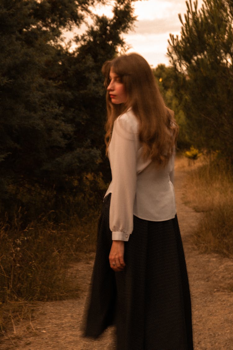 Young Woman In White Blouse And Black Skirt Walking On A Rural Trail