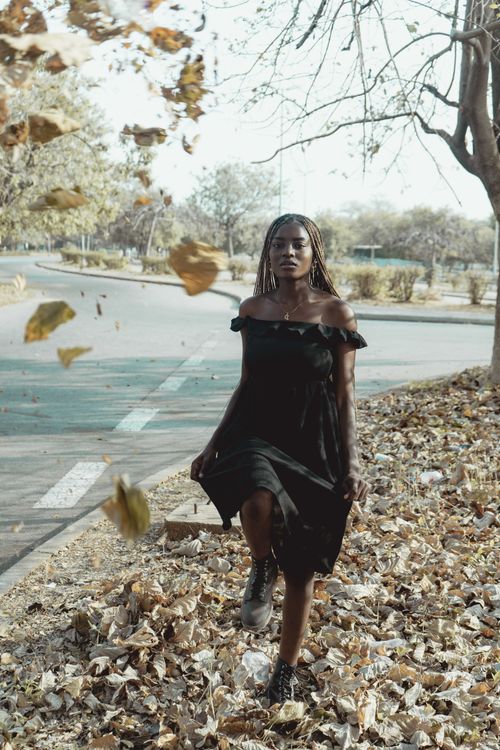 Free A stylish woman in a black dress poses gracefully amidst falling leaves on an autumn day in Abuja. Stock Photo