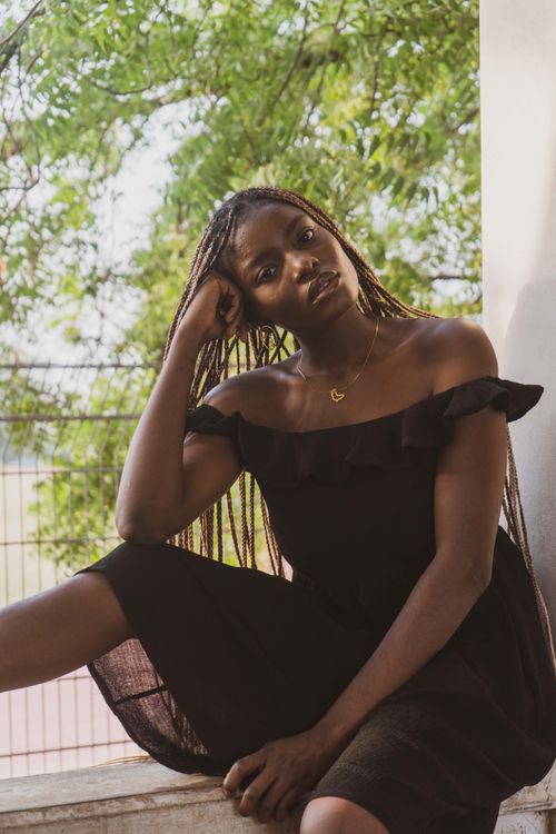 Free Portrait of a woman in a black dress sitting outdoors in Abuja, Nigeria. Stock Photo