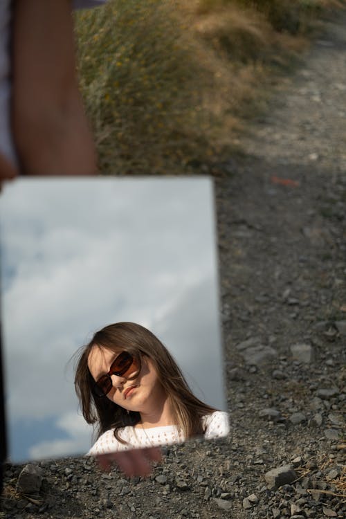 Young Brunette Woman in Sunglasses Reflecting in a Small Mirror
