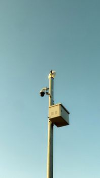 A streetlight pole with surveillance and safety cameras against a clear blue sky.