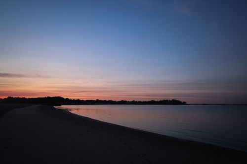 Free A peaceful beach scene at sunset with soft hues in the sky reflecting on calm ocean waters. Stock Photo