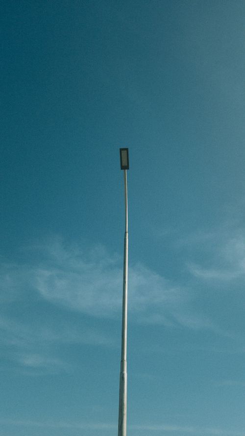 Free Tall street lamp standing against a clear blue sky with scattered clouds. Minimalist and modern. Stock Photo