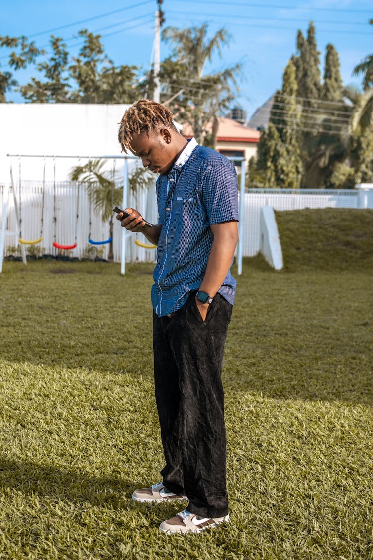 Man In A Blue Shirt And Black Pants Checking His Smart Phone