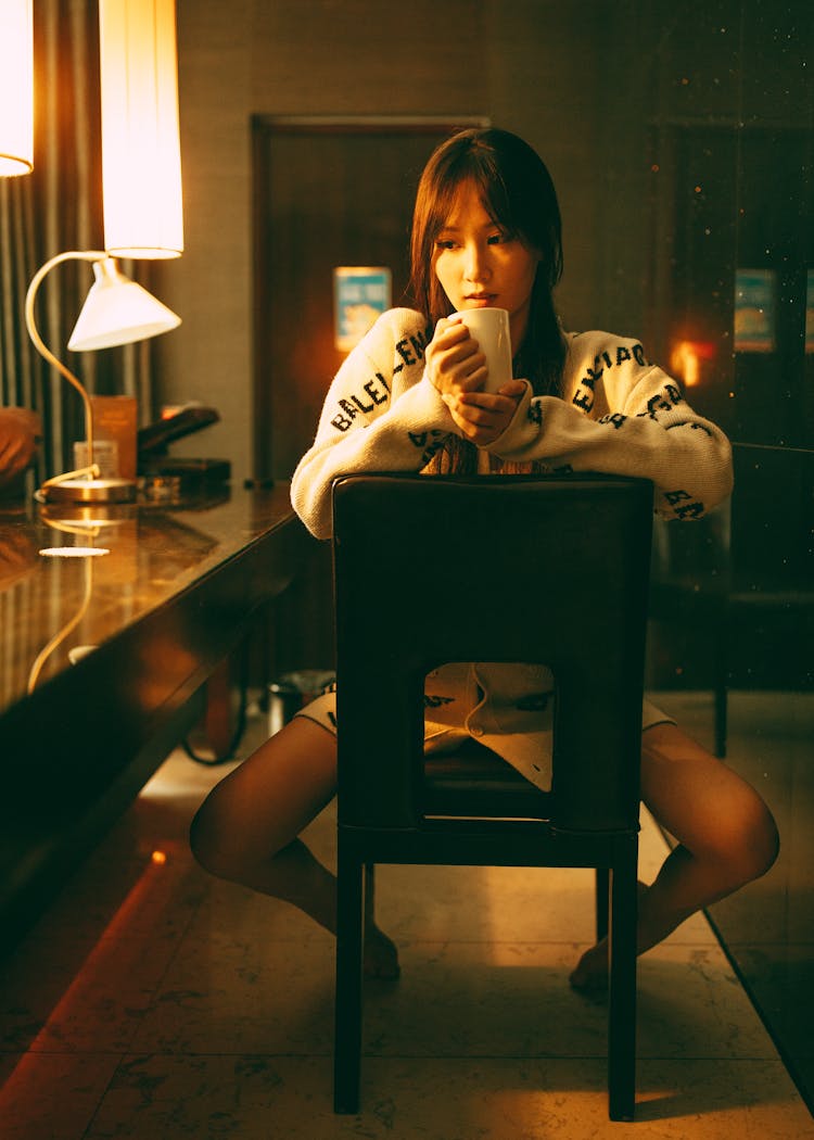 Young Woman Straddling A Chair With A Coffee Cup