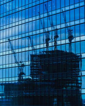 Urban construction cranes reflected on a modern glass facade, creating a dynamic cityscape contrast.