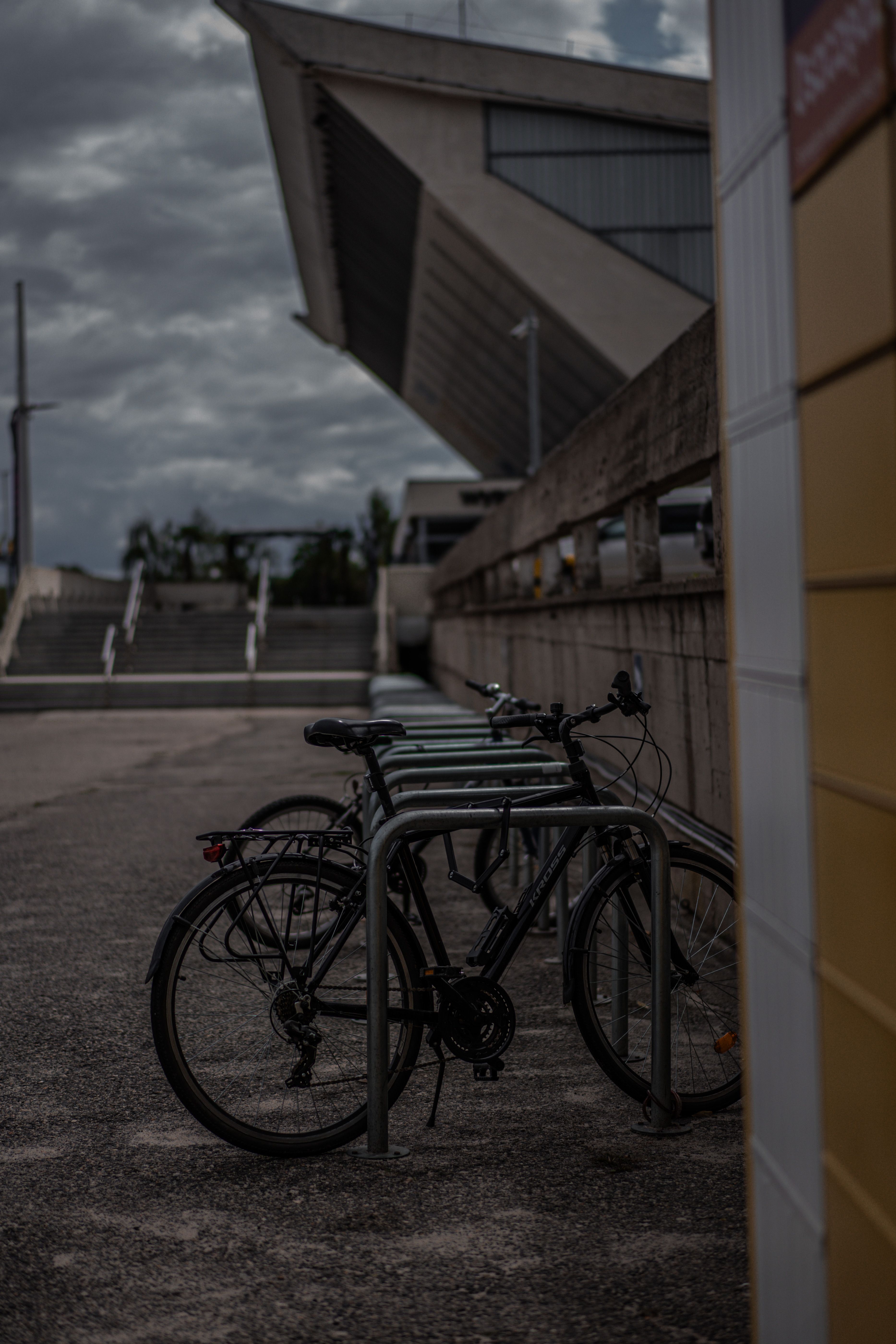 Bicycles parked at a stand near a modern architectural building on an overcast day.