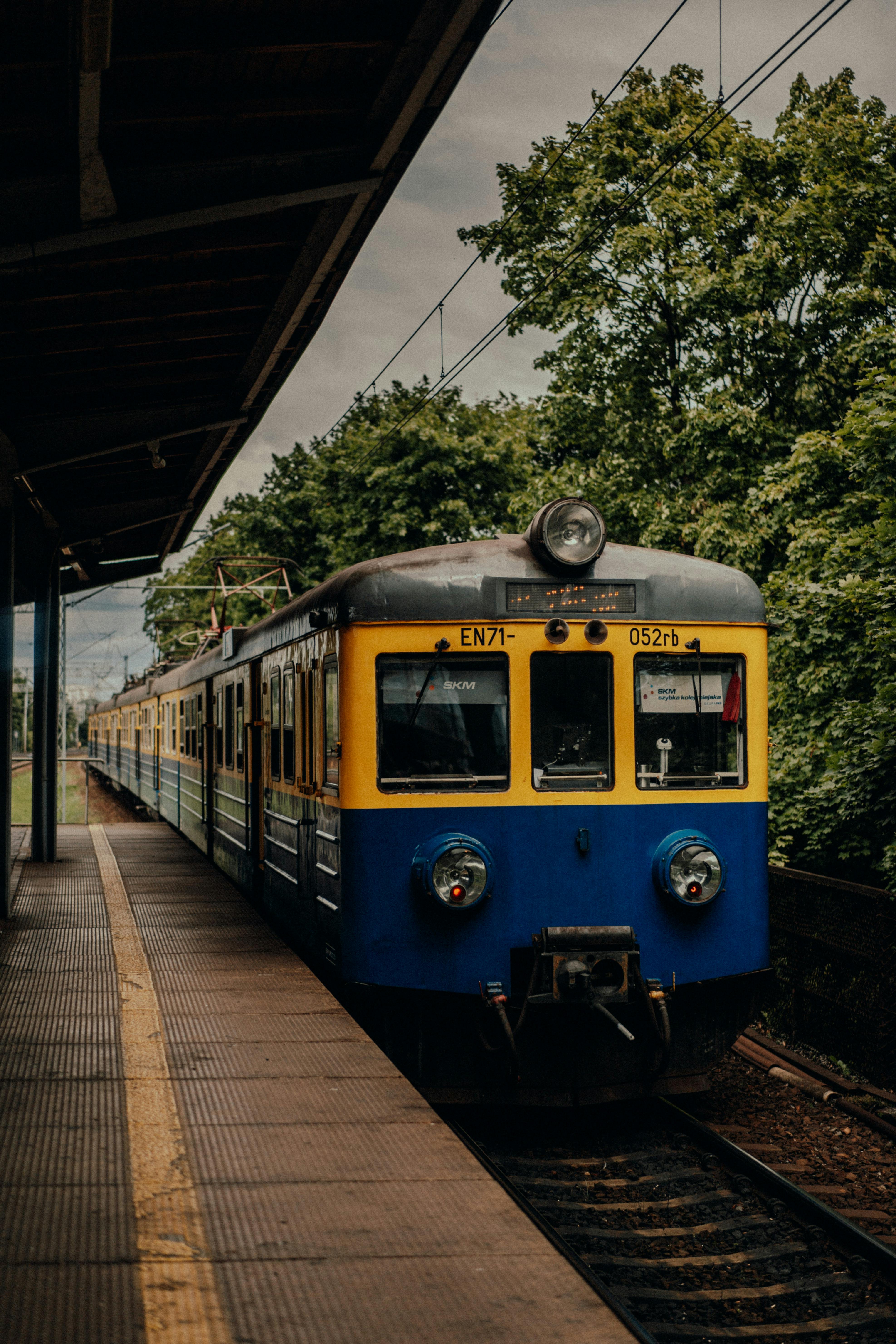 Free A classic train waiting at an urban platform surrounded by lush trees. Stock Photo