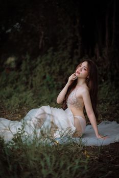 Stunning woman in elegant lingerie poses outdoors, surrounded by lush greenery, showcasing stylish fashion.