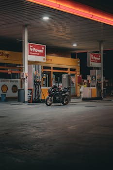 A sport bike parked at a Shell gas station at night, illuminated by neon lights.