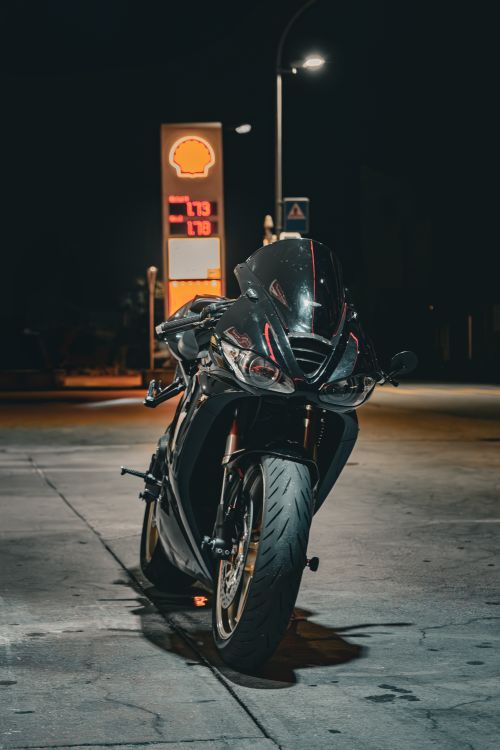 Free A sleek black motorcycle parked at a gas station illuminated by streetlights at night. Stock Photo