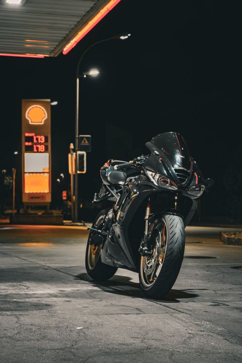 Free Black sport motorcycle parked at a brightly lit gas station at night, urban setting. Stock Photo