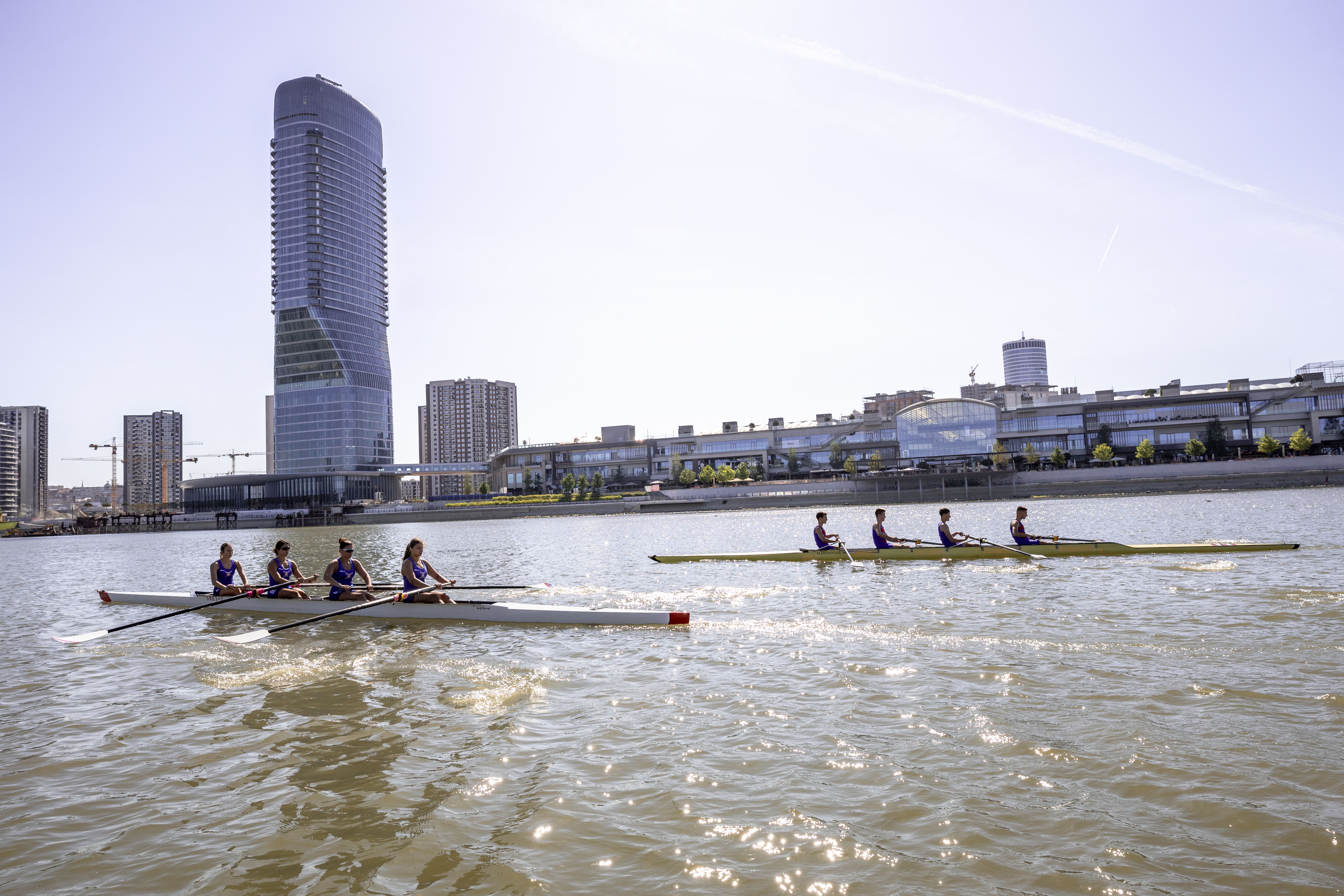Men and Women Rowing in a River, and City Waterfront in Background ...