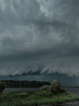 A dramatic storm cloud formation looms over a tranquil lake landscape, creating a striking natural scene.
