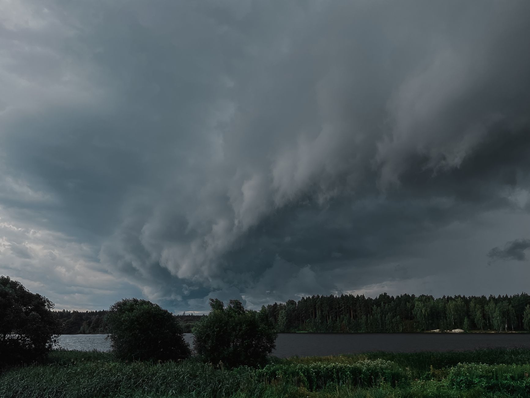 Dark storm clouds gather over a tranquil countryside lake, creating a dramatic and atmospheric scene.