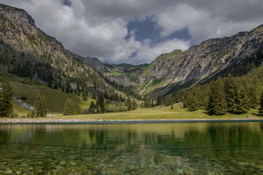 A scenic mountain range reflected in a tranquil alpine lake surrounded by lush greenery.