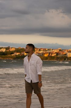 Portrait of a man in a white shirt walking along a scenic beach coast during sunset.