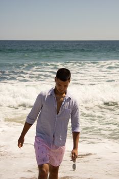 Man walking on beach in casual summer attire. Embracing relaxation by the sea.