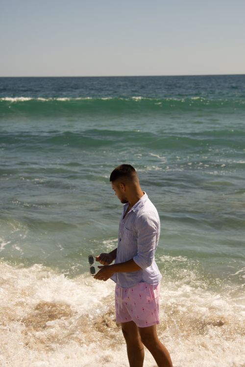 Free A man stands by the ocean shore in a casual outfit enjoying a sunny day. Stock Photo