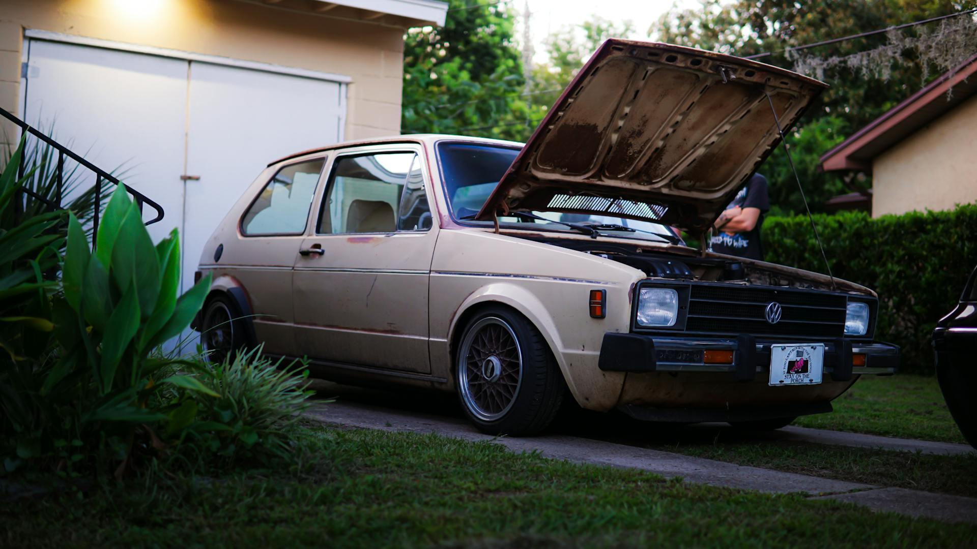 Classic Volkswagen car with open hood parked in a suburban setting, showcasing its vintage charm.