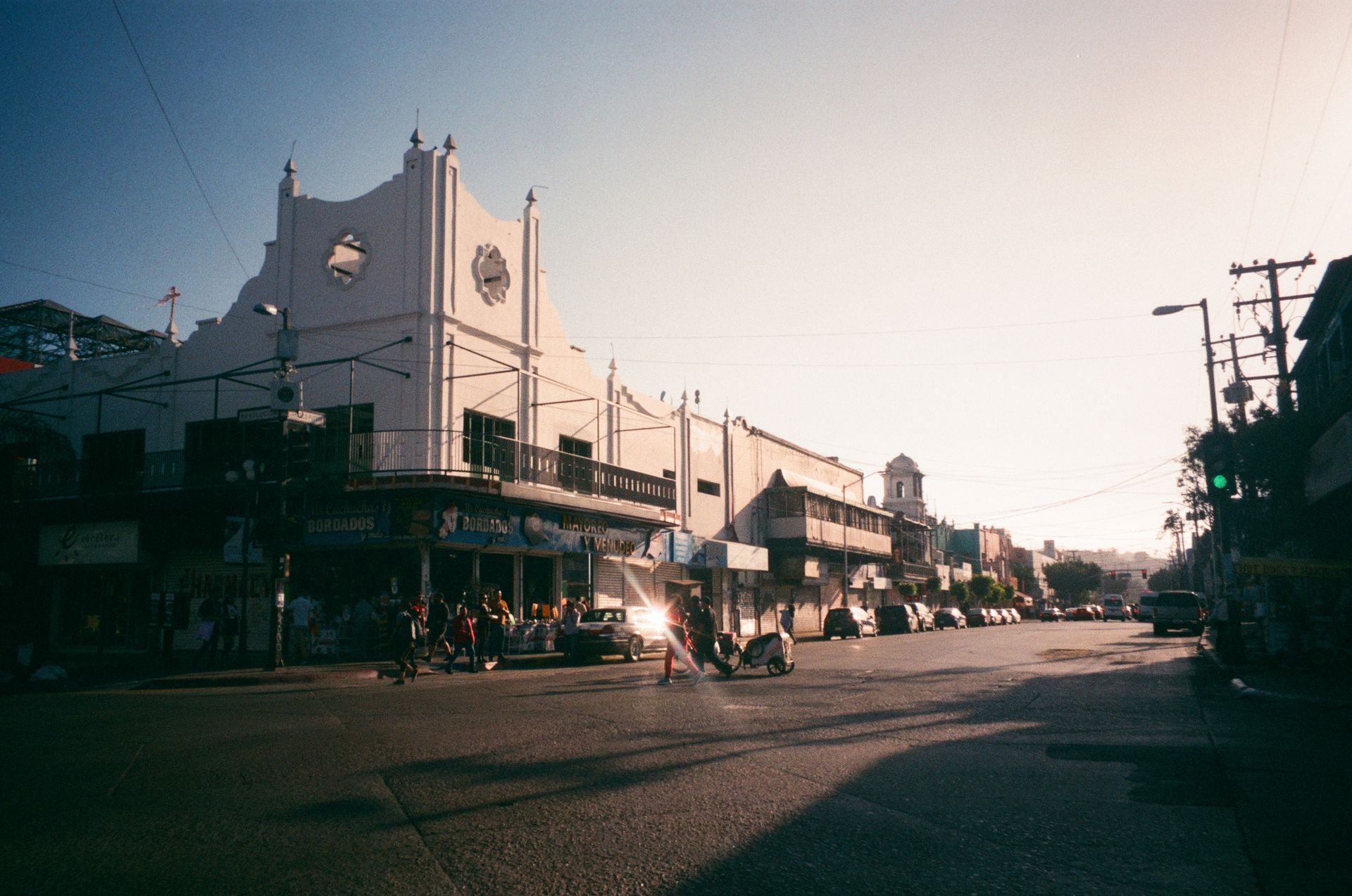 A sunlit street corner in Tijuana, Mexico with historic architecture and urban activity.