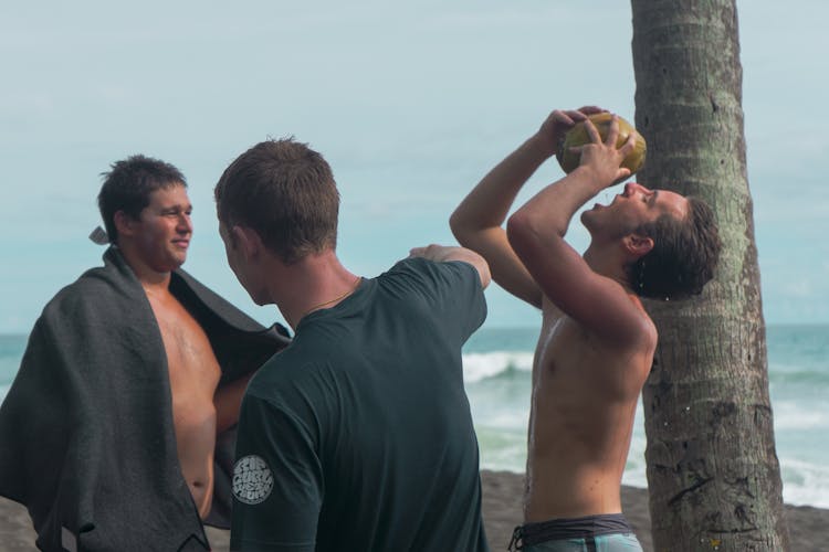 Young Men Drinking From Coconuts On Beach