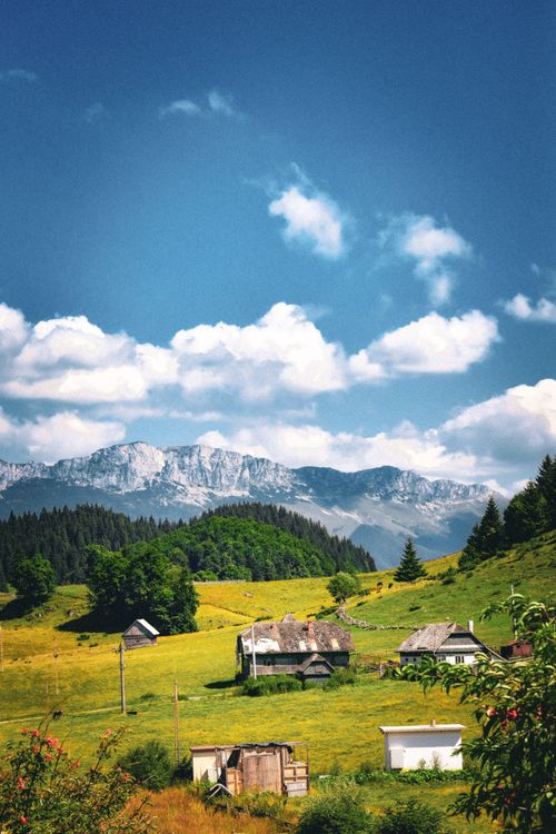 Free Charming countryside view with rustic houses, green fields, and majestic mountains. Stock Photo