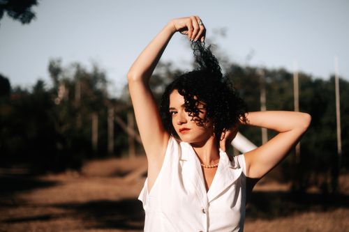 Free A young woman with curly hair poses outdoors in the countryside during sunset. Stock Photo