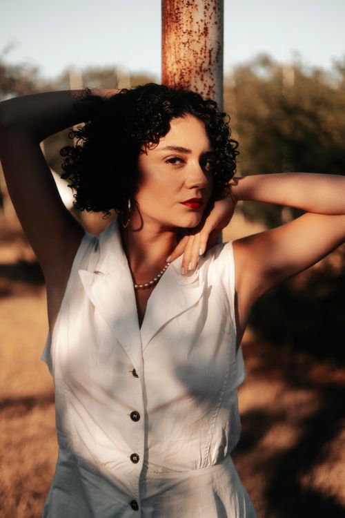 Free Stylish outdoor portrait of a woman with curly hair wearing a white shirt, captured in warm natural light. Stock Photo