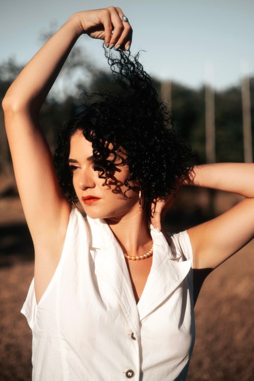 Free A stylish woman posing outdoors with curly hair during a warm sunset, showcasing natural beauty. Stock Photo