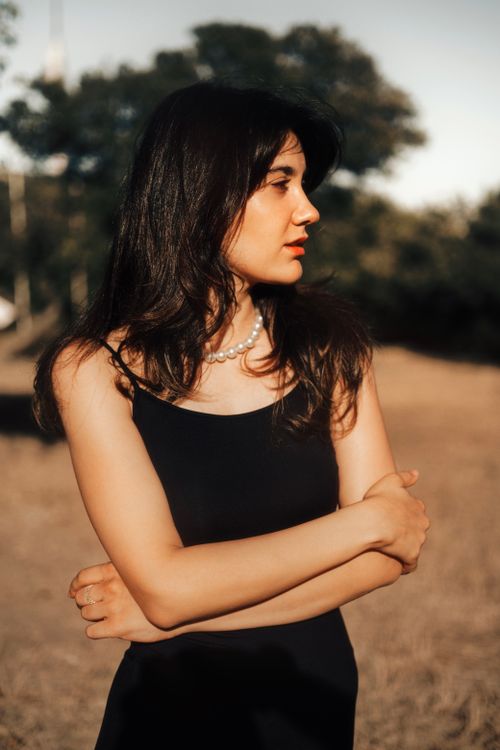 Free Woman in a black dress with pearl necklace poses outdoors in warm sunlight. Stock Photo