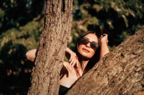 Free Young woman in sunglasses posing by tree in summer sun. Stock Photo