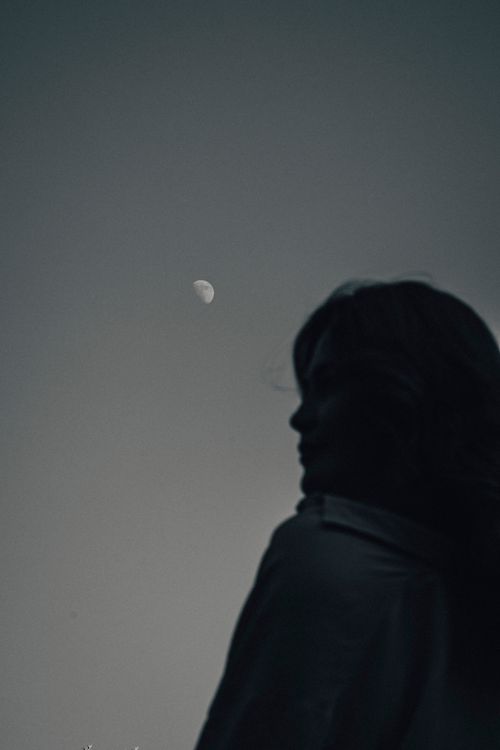 Free A silhouette of a woman gazing at the moon under a clear evening sky. Stock Photo