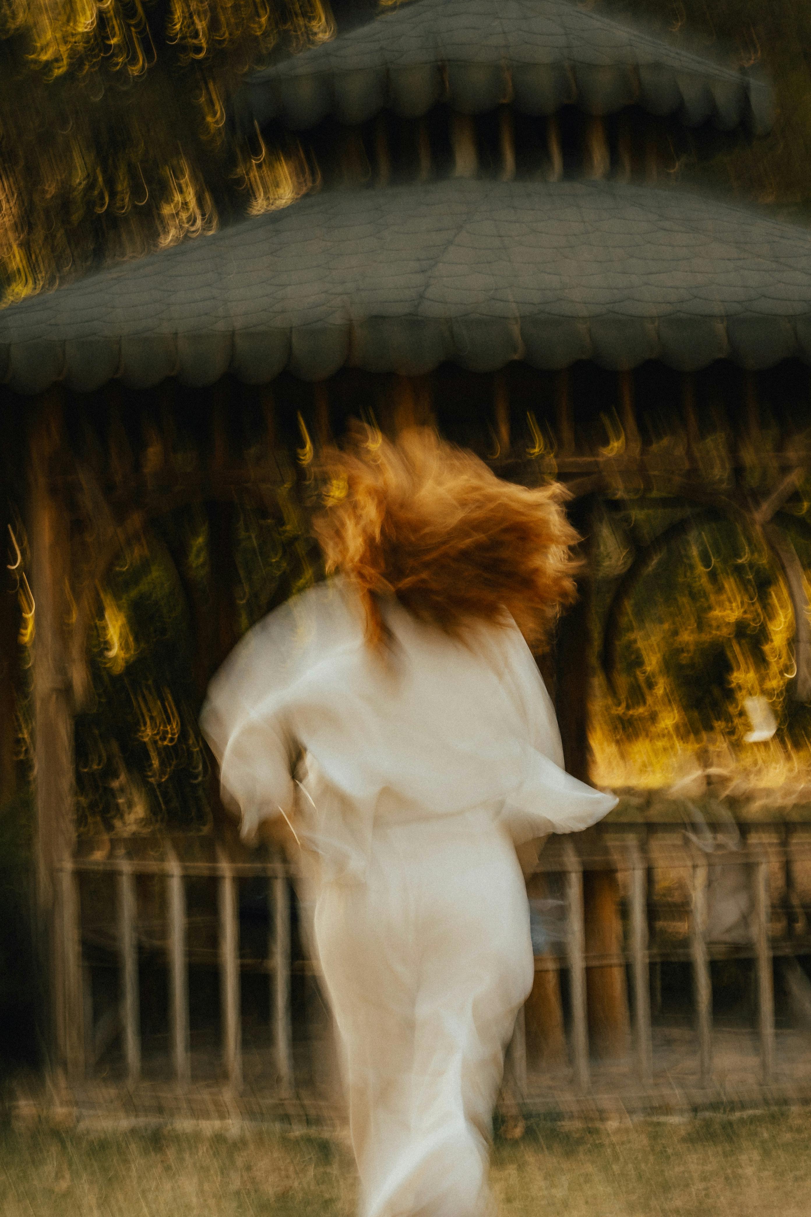 Artistic motion blur photograph of a woman running towards a gazebo in a sunlit park.