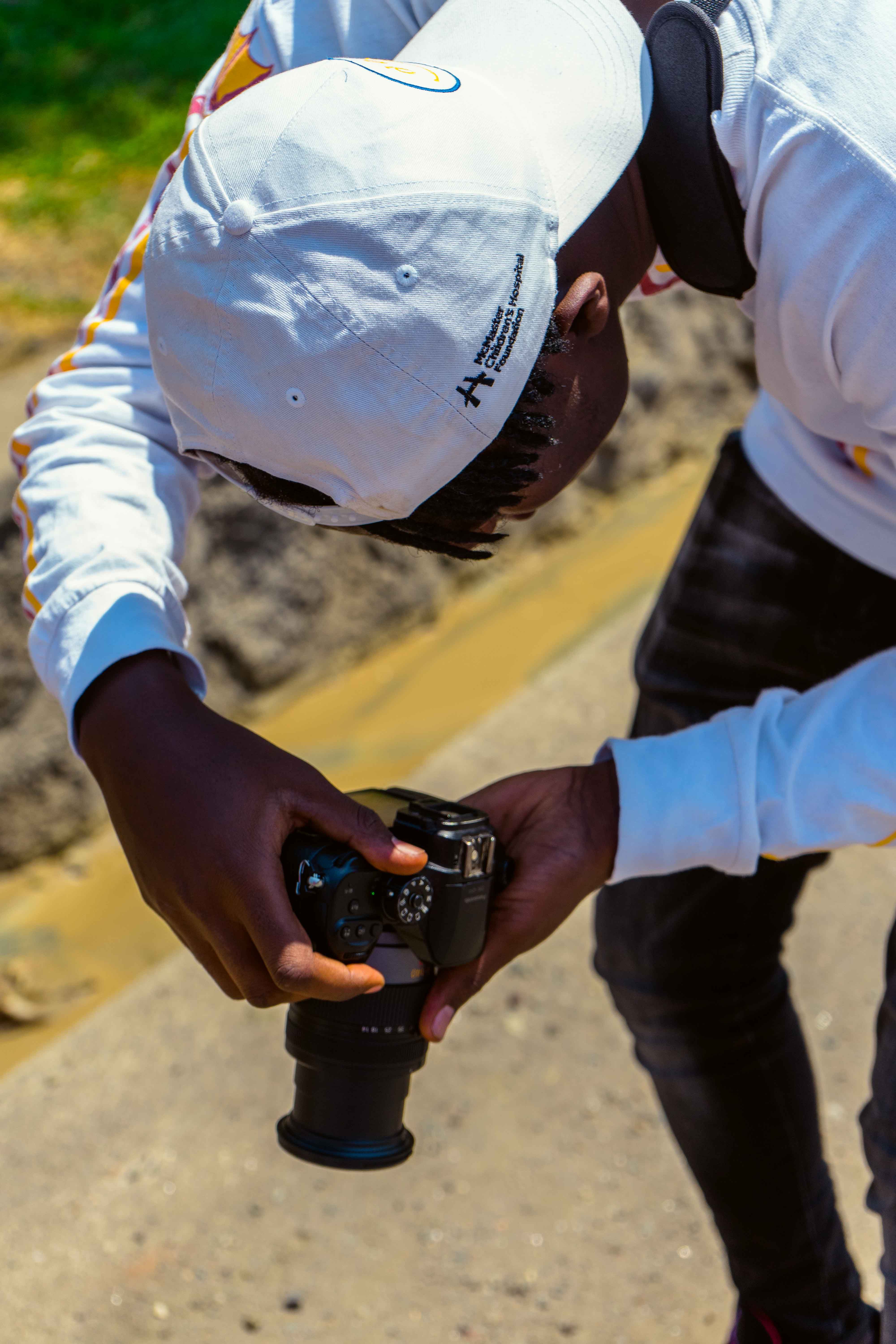 Black man skillfully uses a camera outdoors, highlighting photography as a hobby.