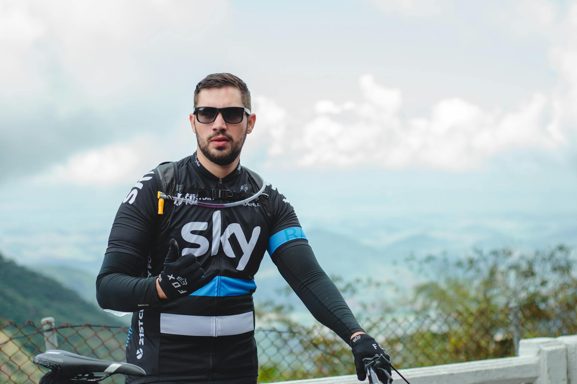 Portrait of a male cyclist in Team Sky jersey with sunglasses, captured outdoors with scenic background.