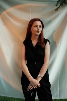 Portrait of a redhead woman standing elegantly in a black outfit with a soft background.