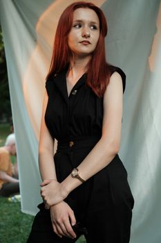 Fashionable young woman with red hair posing elegantly outdoors against a white backdrop.