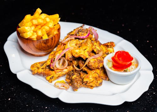 Free Savor spicy chicken wings with crispy fries and a fresh salad on a stylish plate. Stock Photo