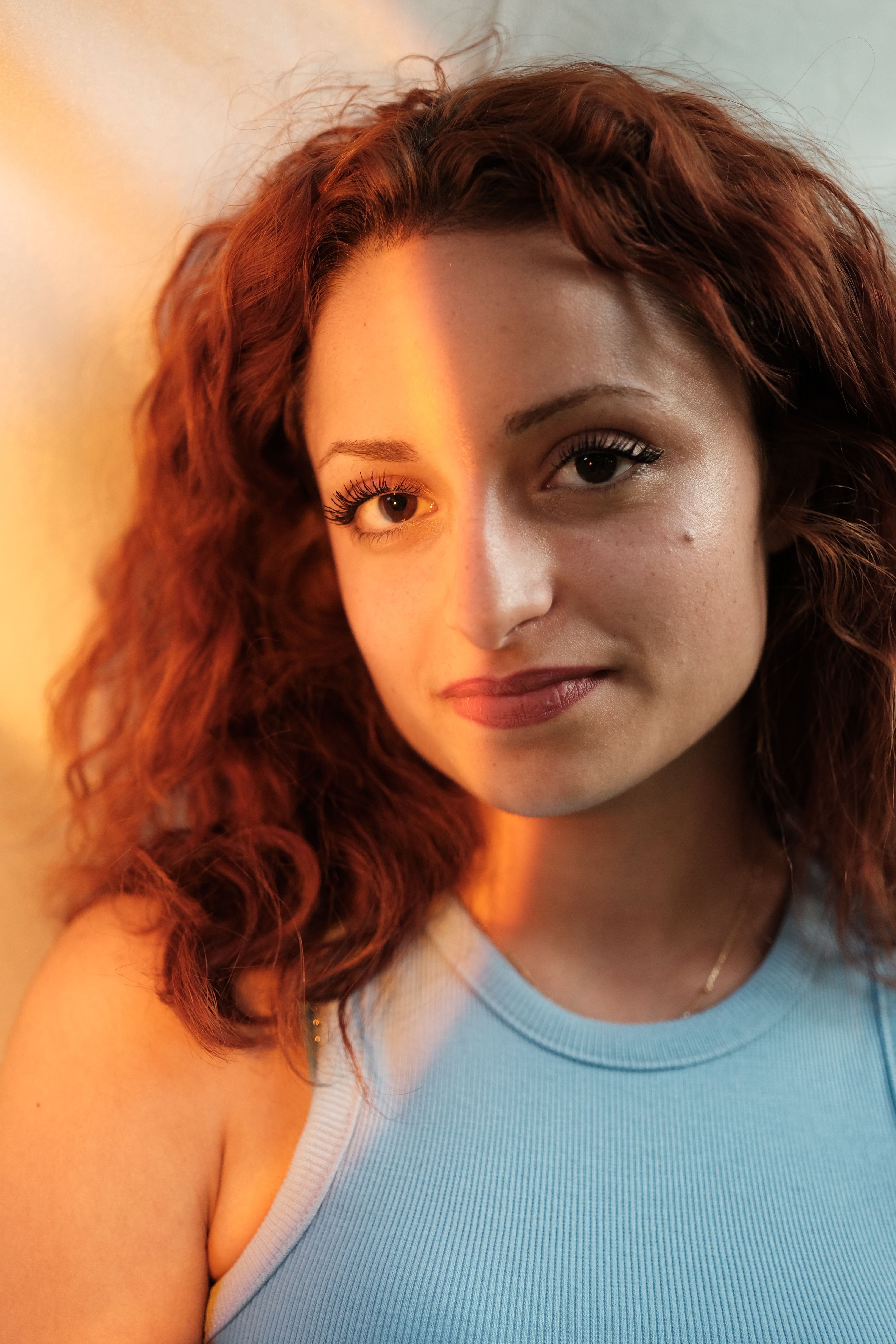 Portrait of a young woman with red hair in soft golden light, wearing blue.