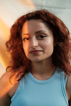 Close-up of a woman with red hair smiling in a soft natural light setting.