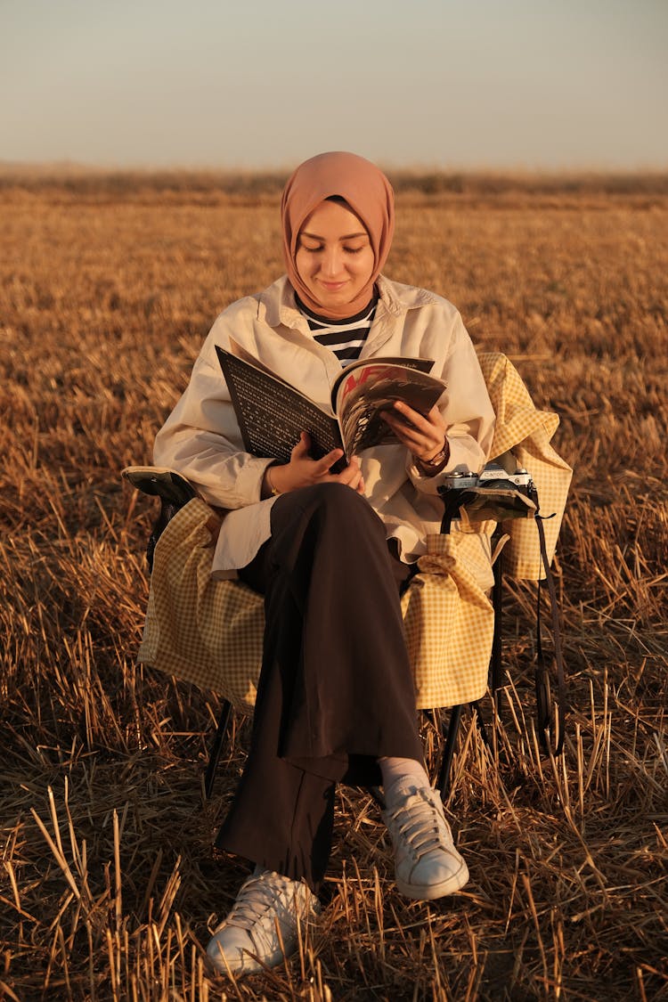 Woman Reading Magazine On Field At Sunset